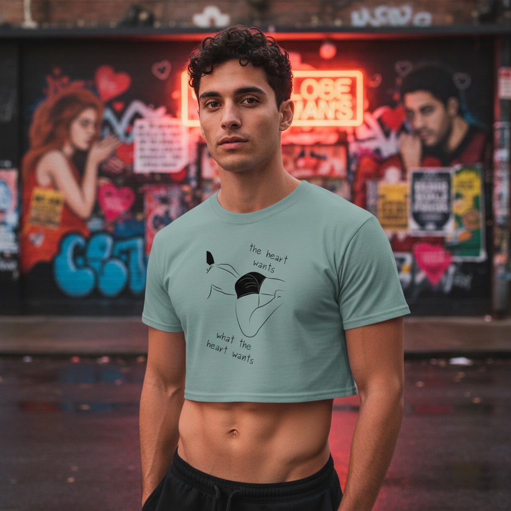 Pale green crop top with "The Heart Wants What The Heart Wants" and a minimalist face, worn by a young man near graffiti.