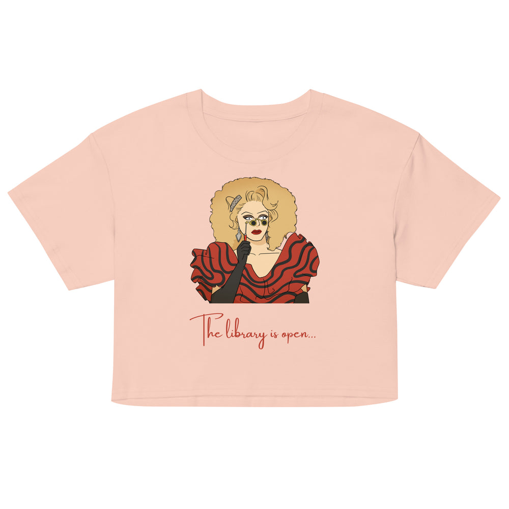 Front view of a pink crop top with a drag performer illustration and “The library is open...” text