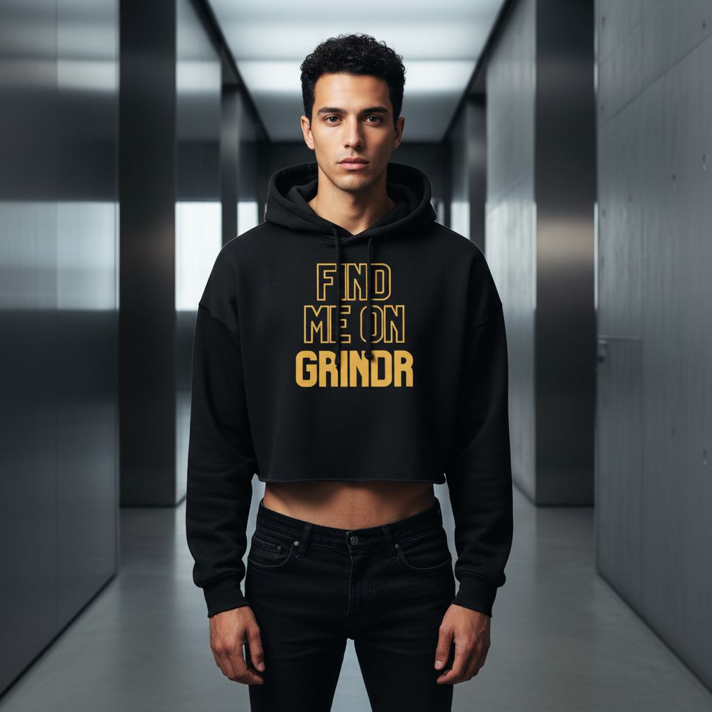 Find Me On Grindr Crop Hoodie with bold yellow text, rocked by a young man in a shiny metallic hallway, queer fashion vibes.
