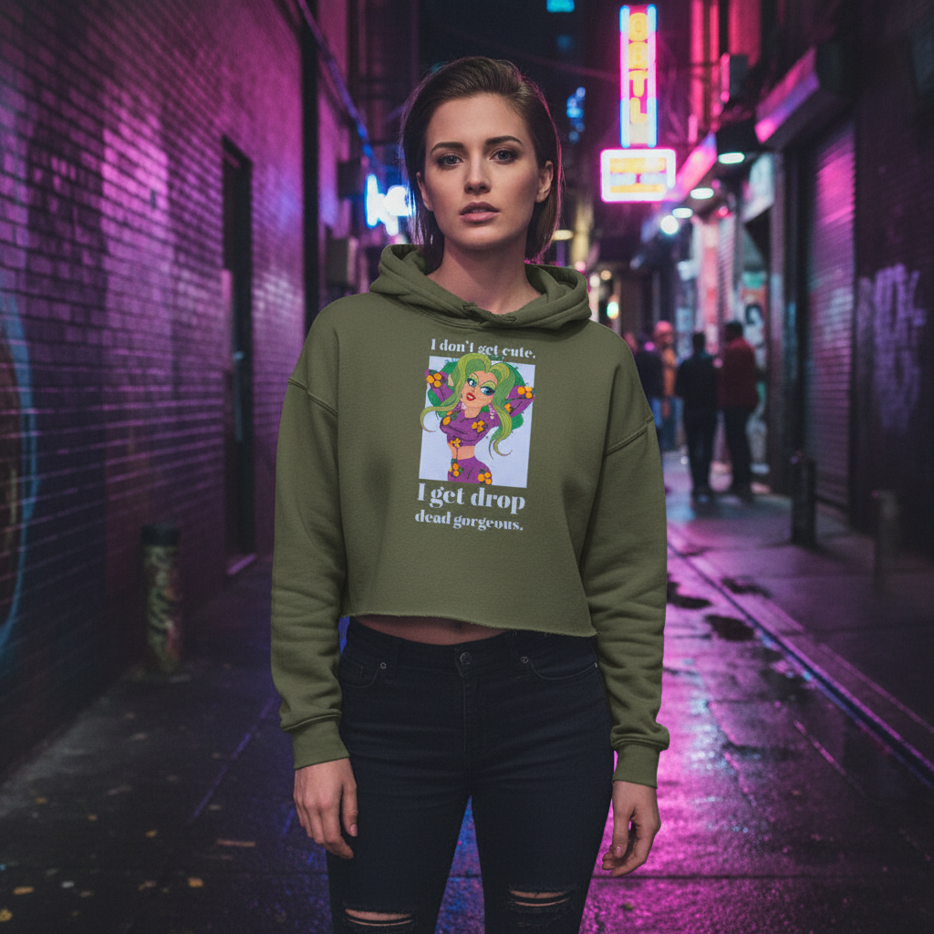 I Get Drop Dead Gorgeous" crop hoodie with a colorful cartoon and the phrase: I don't get cute, I get drop dead gorgeous; neon pink and blue night lights shine on a confident woman with short hair in an urban alley.