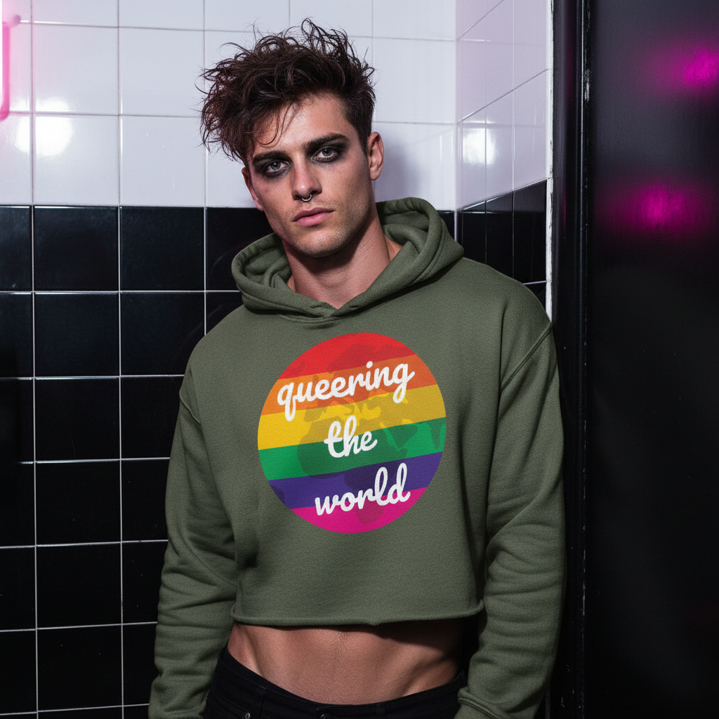 Queering The World Crop Hoodie with rainbow circle and “queering the world” slogan, worn by person on neon-lit black and white tiles.