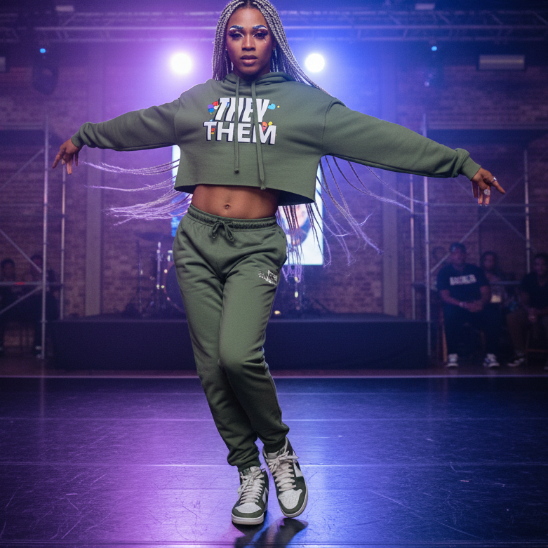 They/Them Crop Hoodie in bold, colorful "THEY/THEM" lettering, worn by a dancer with braids and paired olive green pants.