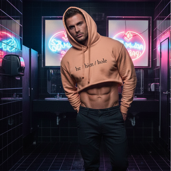 He / Him / Hole Crop Hoodie in a neon-lit, black-tiled restroom; queer man with short hair flaunts abs and dark pants.