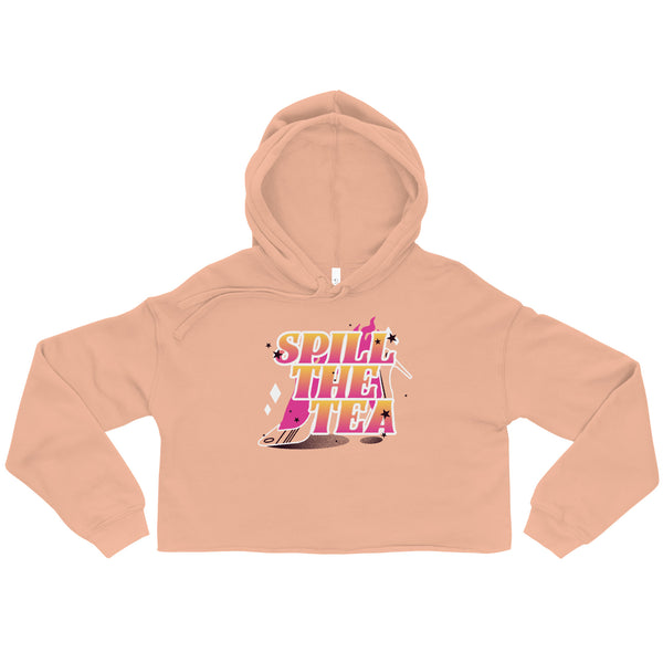 Cropped peach hoodie with SPILL THE TEA in gradient pink-to-yellow, featuring a tipped teacup illustration. Celebrates queer pride and self-expression with bold, empowering style from Queer In The World.