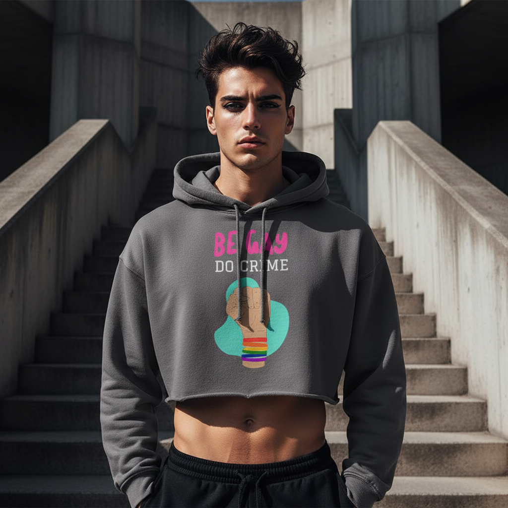 Be Gay Do Crime crop hoodie with rainbow-bracelet fist graphic, worn by a young man in black sweats, exuding queer pride.