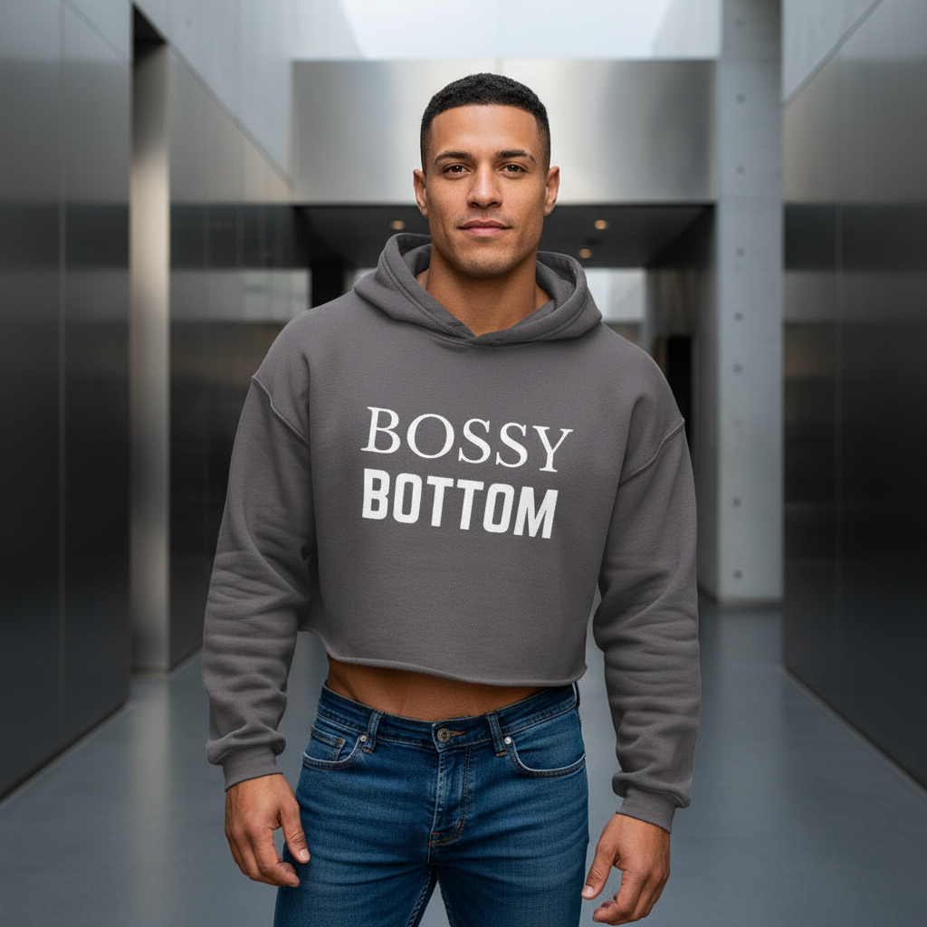 Bossy Bottom Crop Hoodie, gray with bold "BOSSY BOTTOM" in white, worn by a muscular man in jeans. Queer pride look, front-facing.