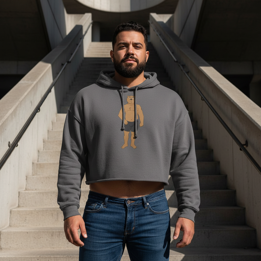 Gray Gay Cub Crop Hoodie with cartoon caveman graphic, worn by a bearded man in blue jeans on sunlit concrete stairs.