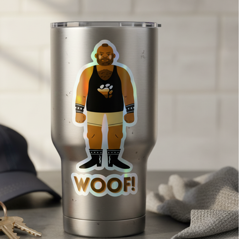Silver tumbler with a holographic “WOOF!” Gay Bear sticker of a bearded wrestler in black gear; cap, keys, cloth rest nearby.