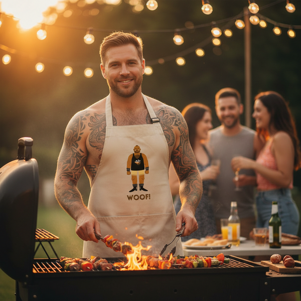 Tattooed person wearing a beige Woof! bear-print apron while grilling skewers at a backyard party