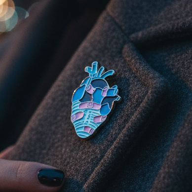 Wounded heart enamel pin with blue, purple, and pink striped heart design on dark fabric