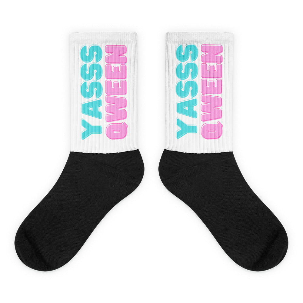 Pair of crew socks with black feet and white ribbed cuffs reading “YASSS QUEEN” in turquoise and pink
