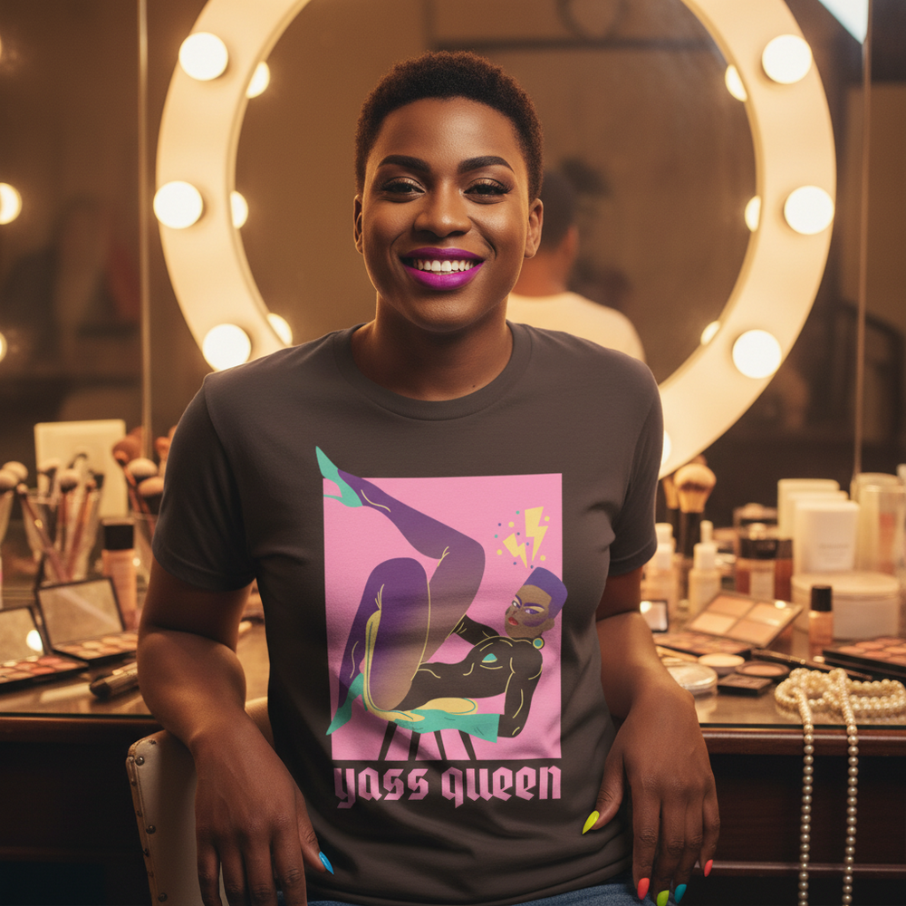 Yass Queen T-shirt with drag queen art and text “yass queen,” worn by a short-haired person amid makeup, pearls