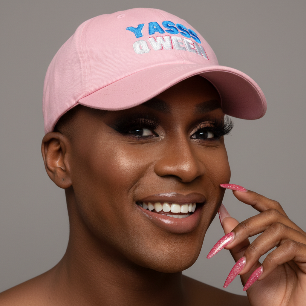 Pink pride dad hat with “YASS QWEEN” in blue and white, worn by glam person with pink nails and bold makeup
