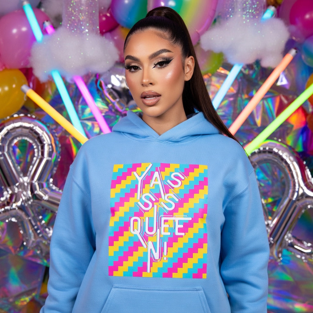 Yasss Queen Unisex Hoodie with bold geometric “I AM QUEEN” print, worn by model amid neon lights and party balloons