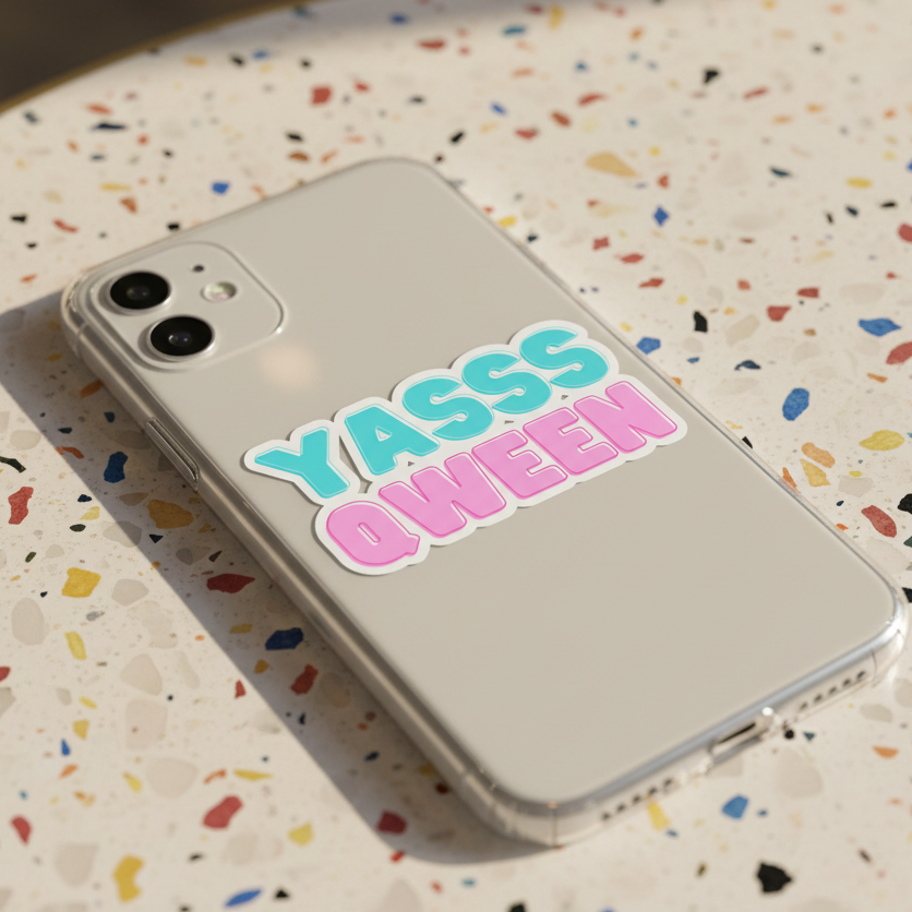 White smartphone in a clear case on terrazzo, sporting a "YASSS QWEEN" sticker in bold teal and pink queer-friendly block