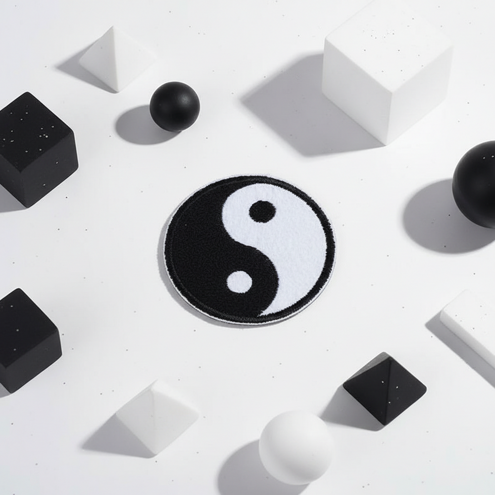 Yin and Yang iron-on embroidered patch sits on white, framed by black and white 3D spheres, cubes, pyramids