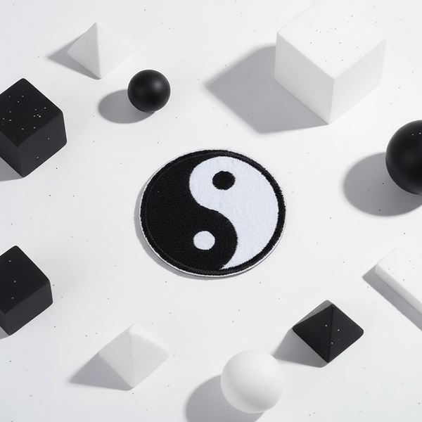 Yin and Yang iron-on embroidered patch sits on white, framed by black and white 3D spheres, cubes, pyramids