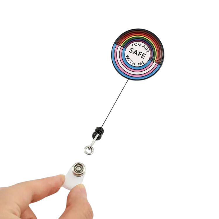 Rainbow-striped retractable badge reel reading “YOU ARE SAFE WITH ME,” with clip held below