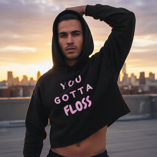 You Gotta Floss Crop Hoodie with bold pink lettering, worn by a young man posing confidently on a city rooftop at sunset.