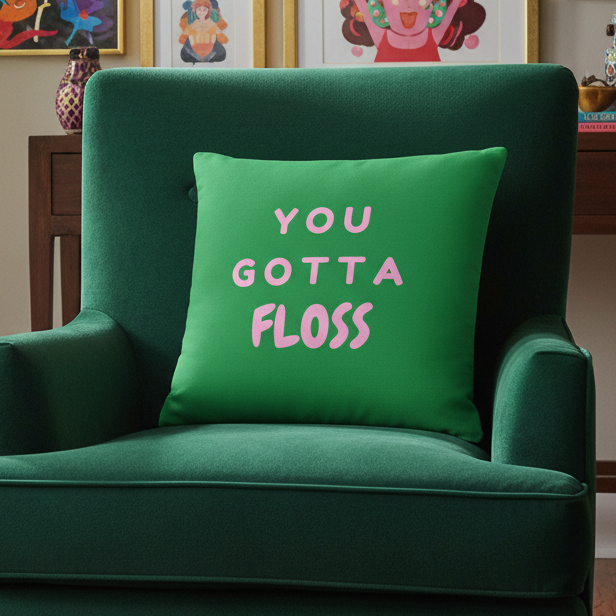 Green armchair with a cushion and pink-and-white "You Gotta Floss Pillow." Wooden table