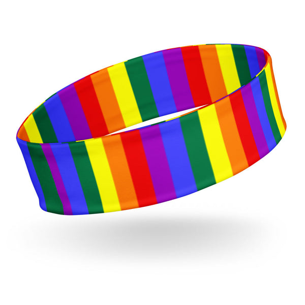 Gay Pride Headband on a person with brown skin and short dark hair, rainbow flags and murals fill the festive Pride street scene behind.