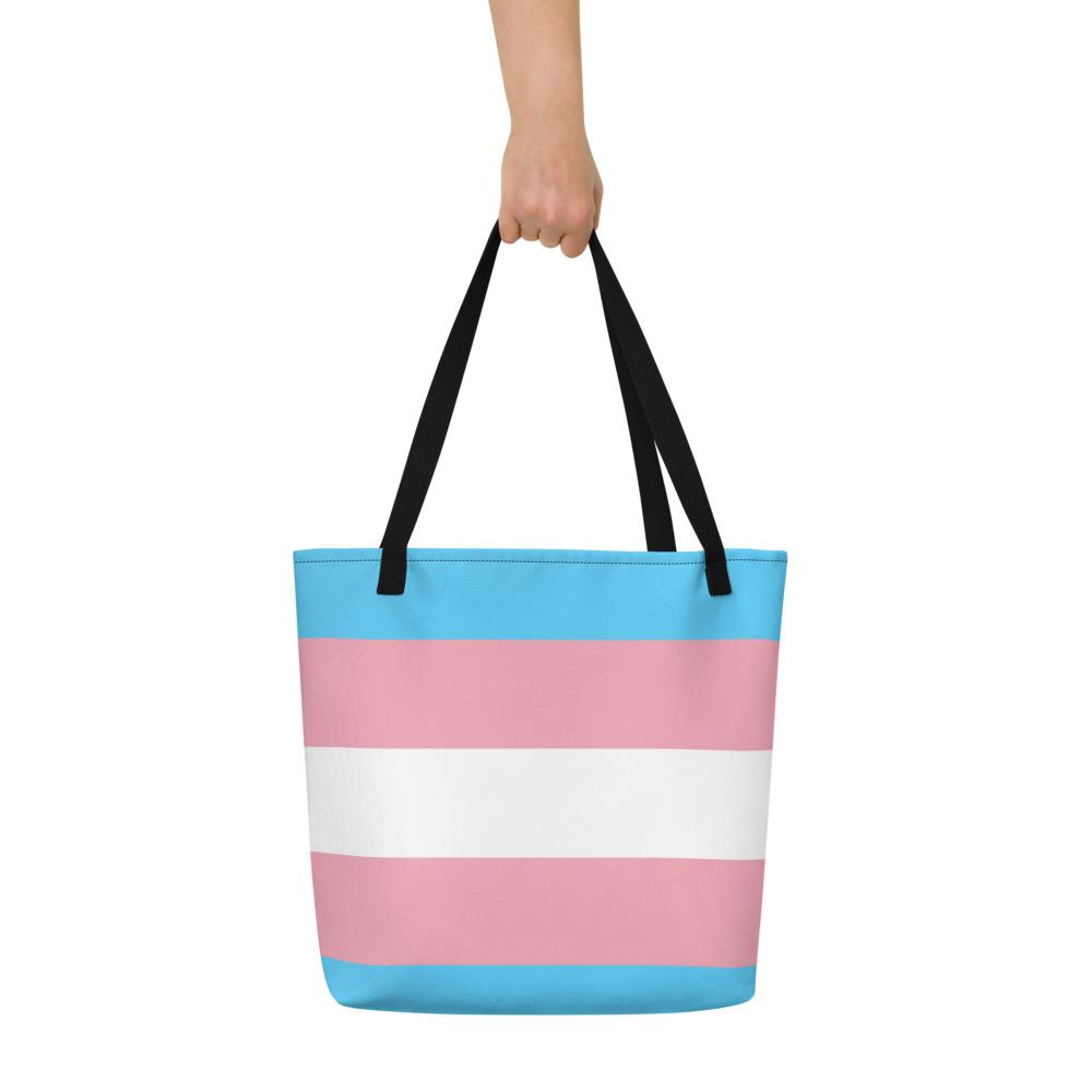Front view of a black-handled tote bag with blue, pink, and white horizontal stripes, held by a hand