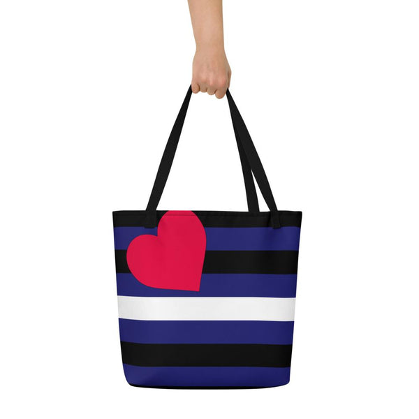 Black tote bag with blue, black, and white stripes and a pink heart, held up by its straps