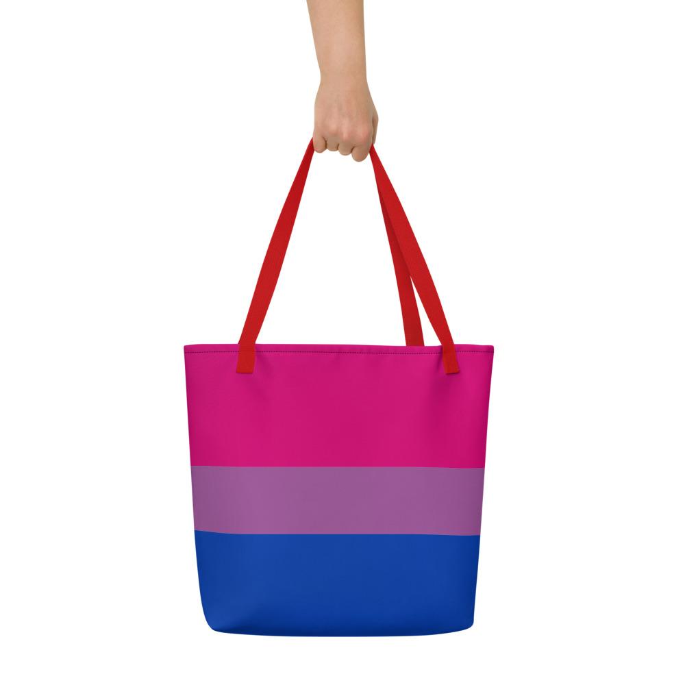 Front view of a large pink, lavender, and blue striped tote bag held by one hand