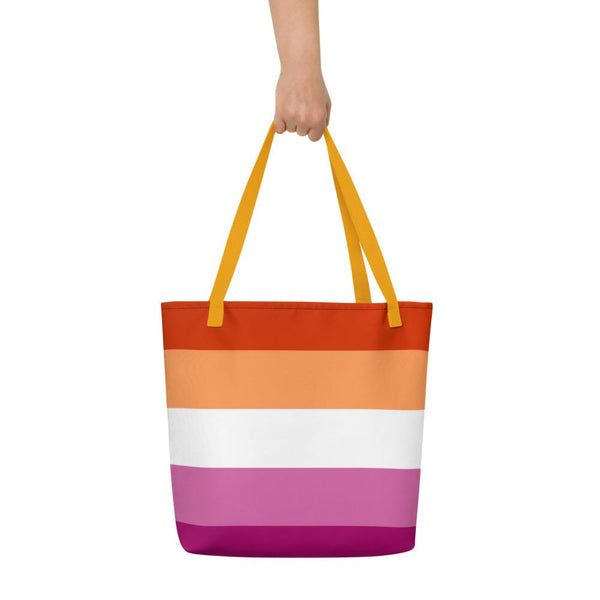 Front view of a striped lesbian Pride tote bag with yellow handles, held against white