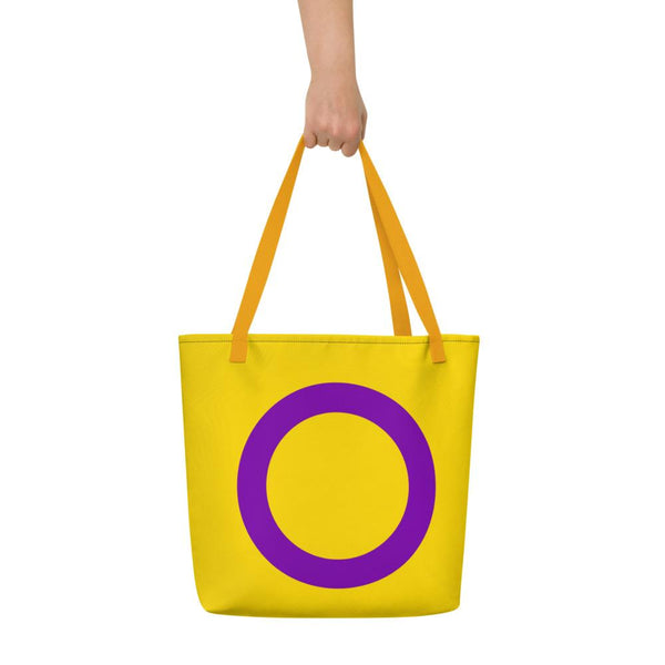 Yellow tote bag with orange handles and a large purple intersex symbol, held by a hand