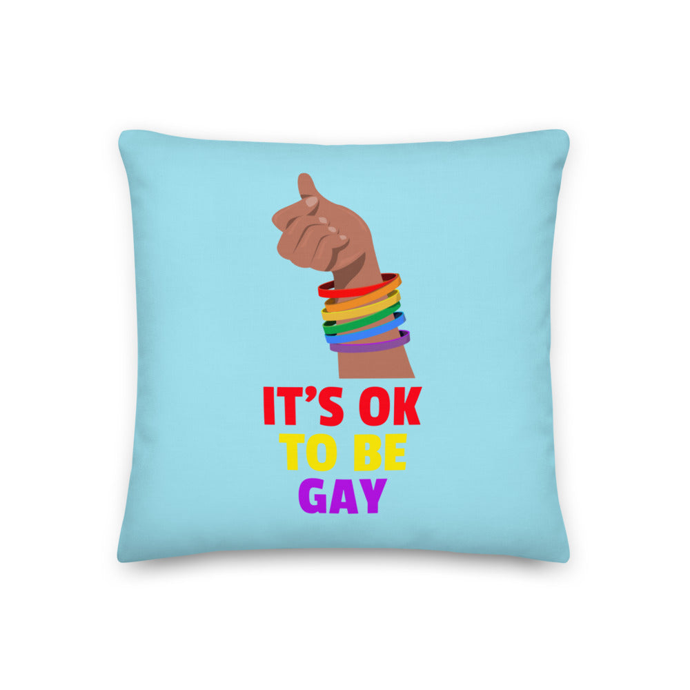 Light blue pillow with rainbow bracelets, a raised hand, and the text “IT’S OK TO BE GAY”