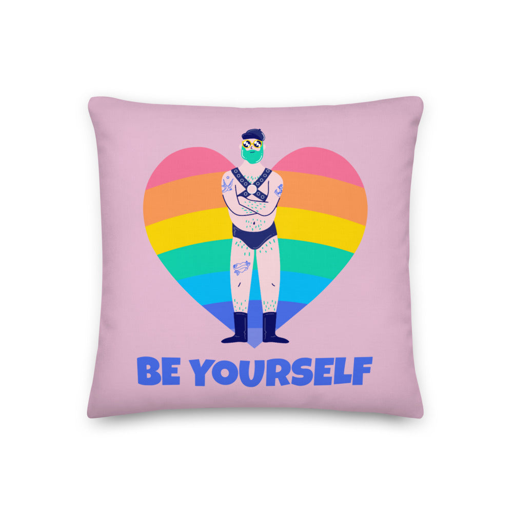 Pink square pillow with a rainbow heart, tattooed underwear-clad figure, and “BE YOURSELF” lettering