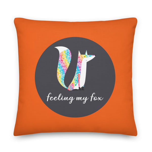 Front view of an orange square pillow with two rainbow-tailed foxes and “feeling my fox” text