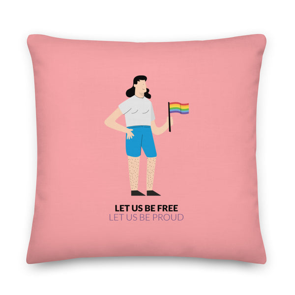 Pink square pillow showing an illustrated person holding a rainbow flag and the words “LET US BE FREE / LET US BE PROUD.”