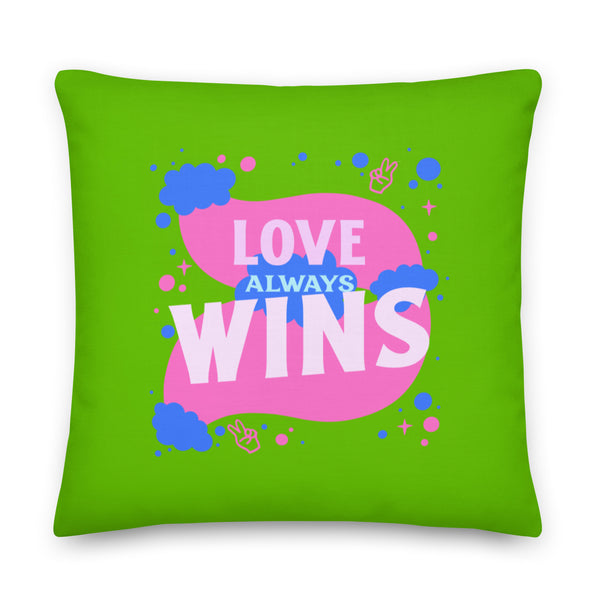 Front view of a bright green square pillow reading “LOVE ALWAYS WINS” in pink and blue