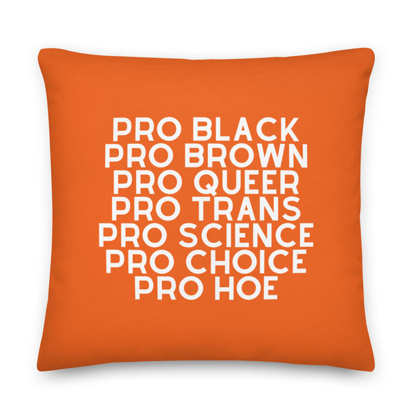 Orange square pillow with white text reading “PRO BLACK, PRO BROWN, PRO QUEER, PRO TRANS, PRO SCIENCE, PRO CHOICE, PRO HOE.”