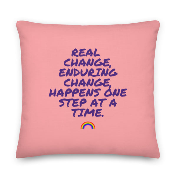 Pink square pillow with purple text reading “Real change, enduring change, happens one step at a time” and a rainbow icon
