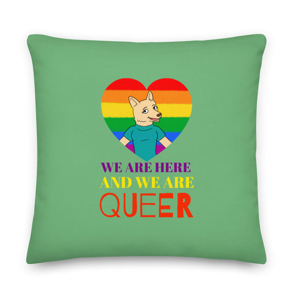Square green pillow with a rainbow heart, cartoon canine, and “WE ARE HERE AND WE ARE QUEER” text