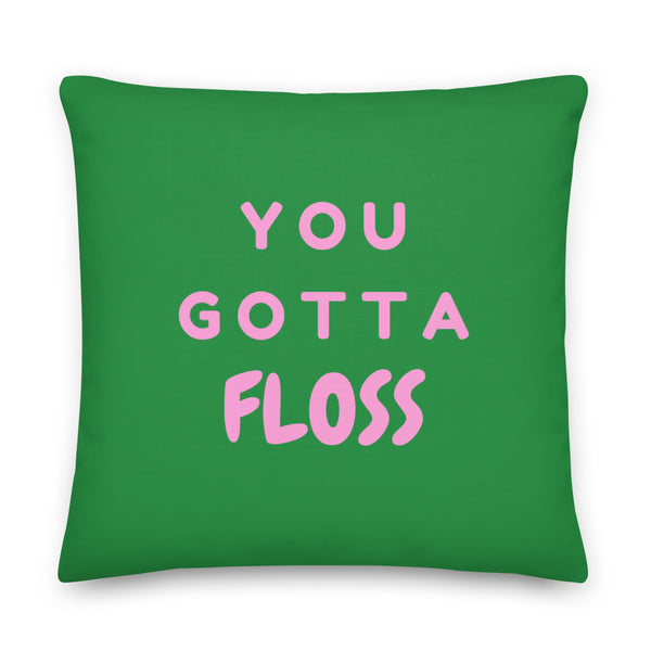 Green square pillow with pink lettering reading “YOU GOTTA FLOSS”