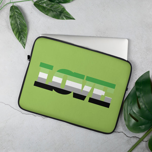 Angled view of a lime-green laptop sleeve with an aromantic pride flag design, beside leaves