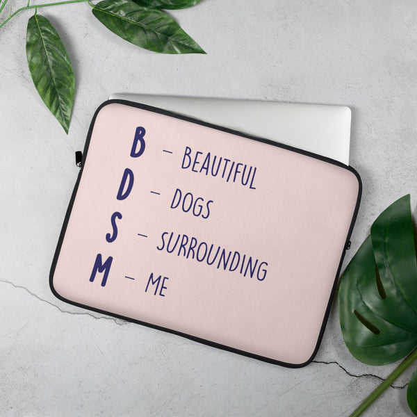 Light pink BDSM (Beautiful Dogs Surrounding Me) laptop sleeve, bold text stacked; queer hand with pastel rainbow nails holds it, silver laptop halfway in.