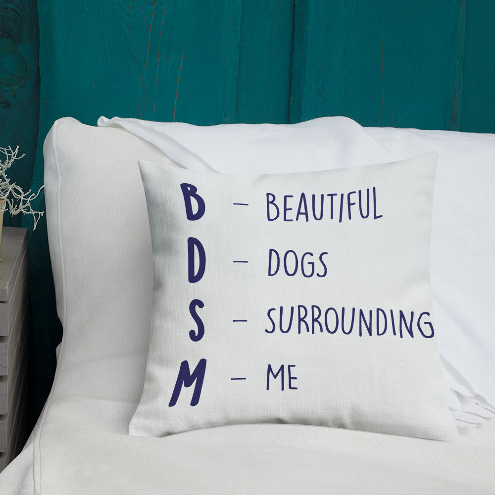 White pillow reading “BDSM — BEAUTIFUL DOGS SURROUNDING ME” on a white bed