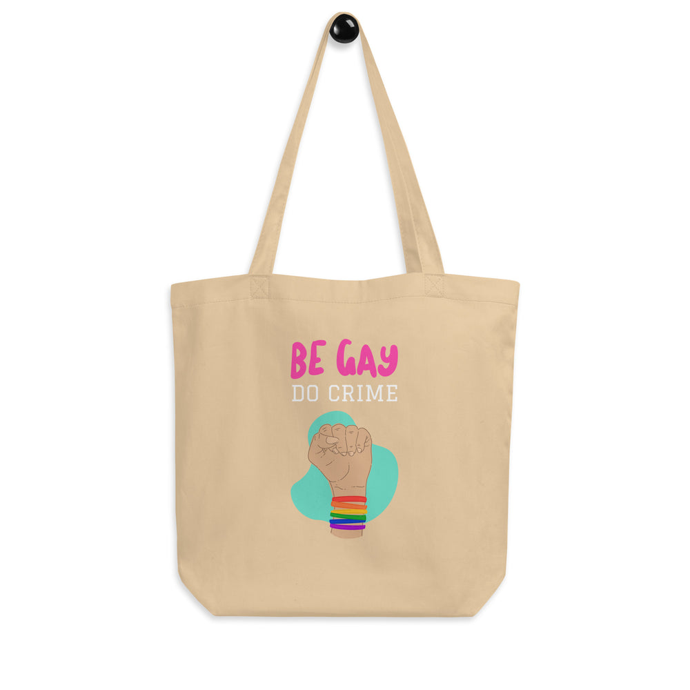 Front-facing beige tote bag reading “BE GAY DO CRIME,” with a rainbow-cuffed raised fist