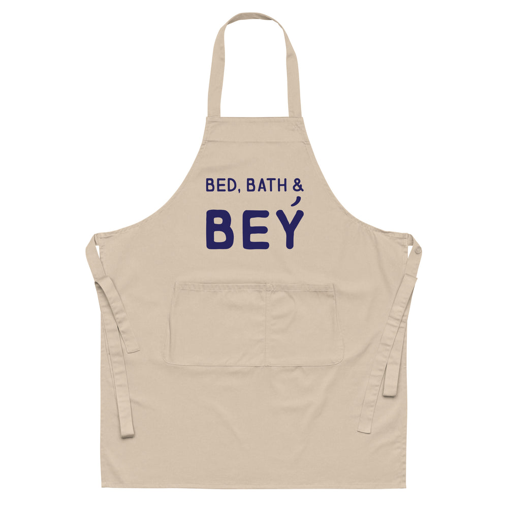 Front-facing beige apron with neck strap, waist ties, pocket, and “BED, BATH & BEY” text