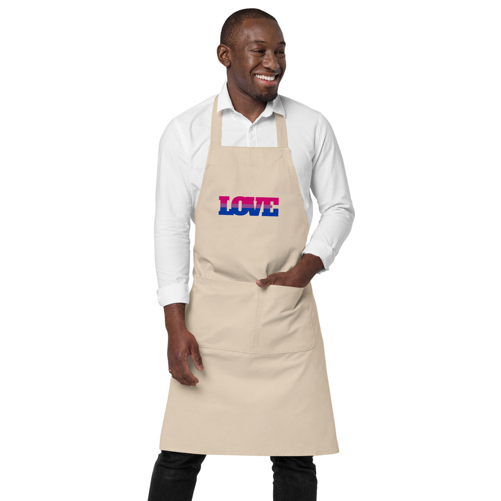 Model wearing a beige apron with a pink-and-blue LOVE graphic and front pocket