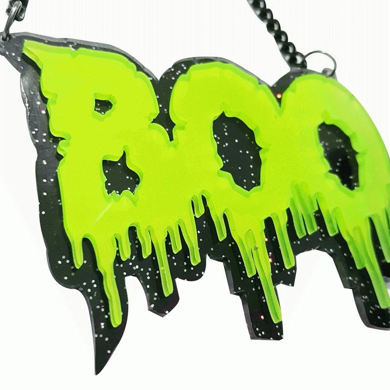 Close-up of a black acrylic BOO statement necklace with neon green dripping letters