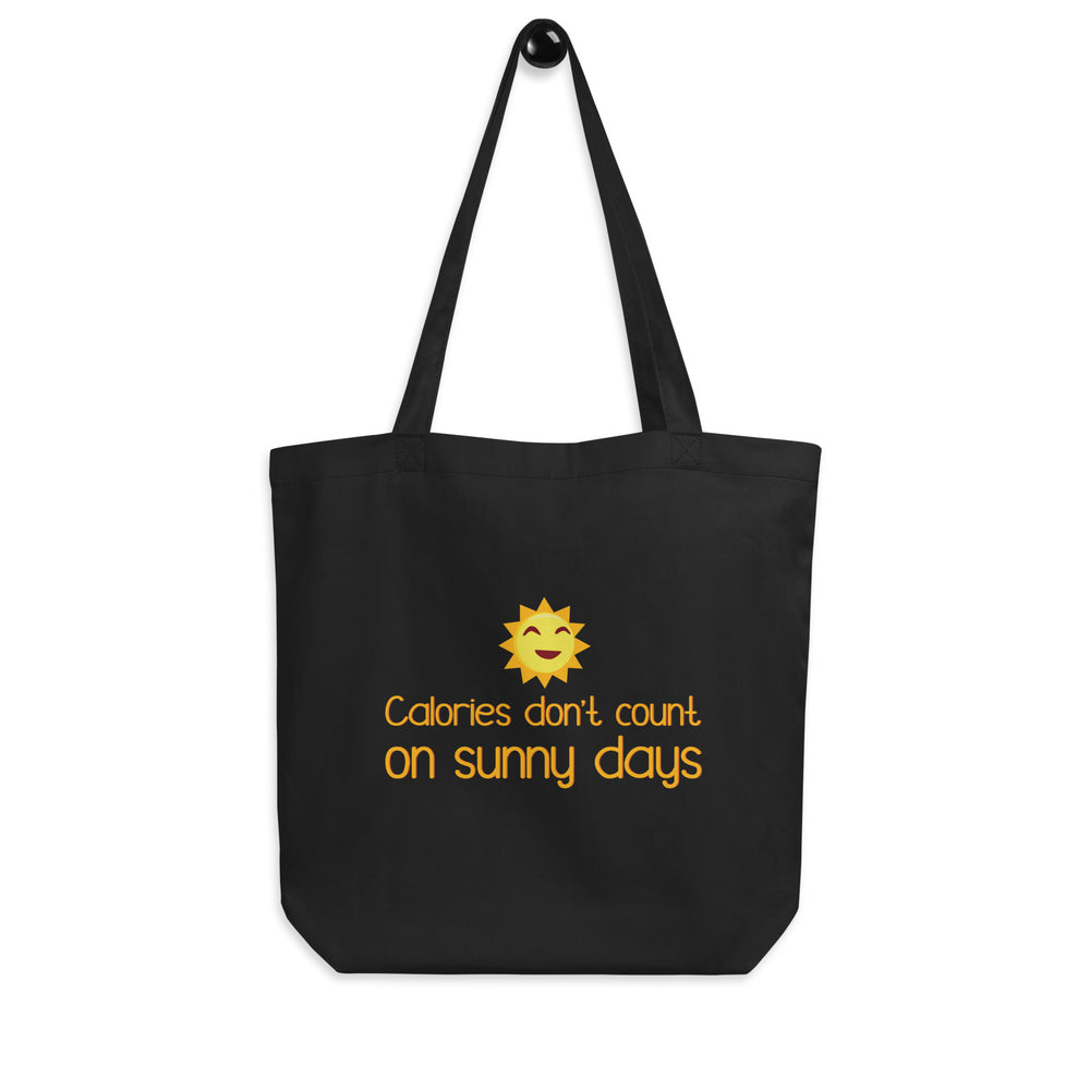 Front view of a black tote bag with a smiling sun and “Calories don’t count on sunny days”