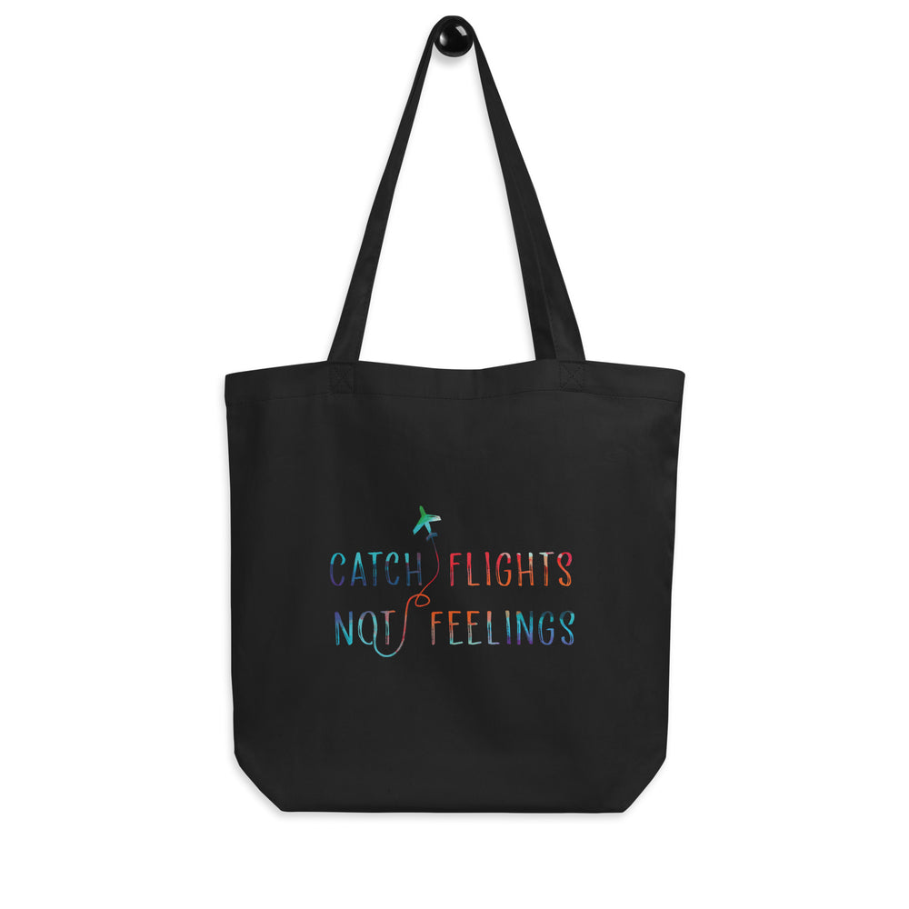 Front view of a black tote bag reading “CATCH FLIGHTS NOT FEELINGS” with a small airplane graphic
