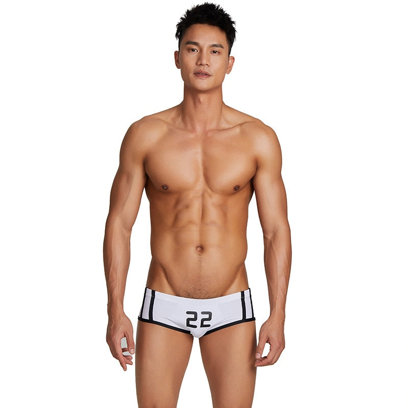 Front-facing model wearing white athletic swim briefs with black trim and number 22