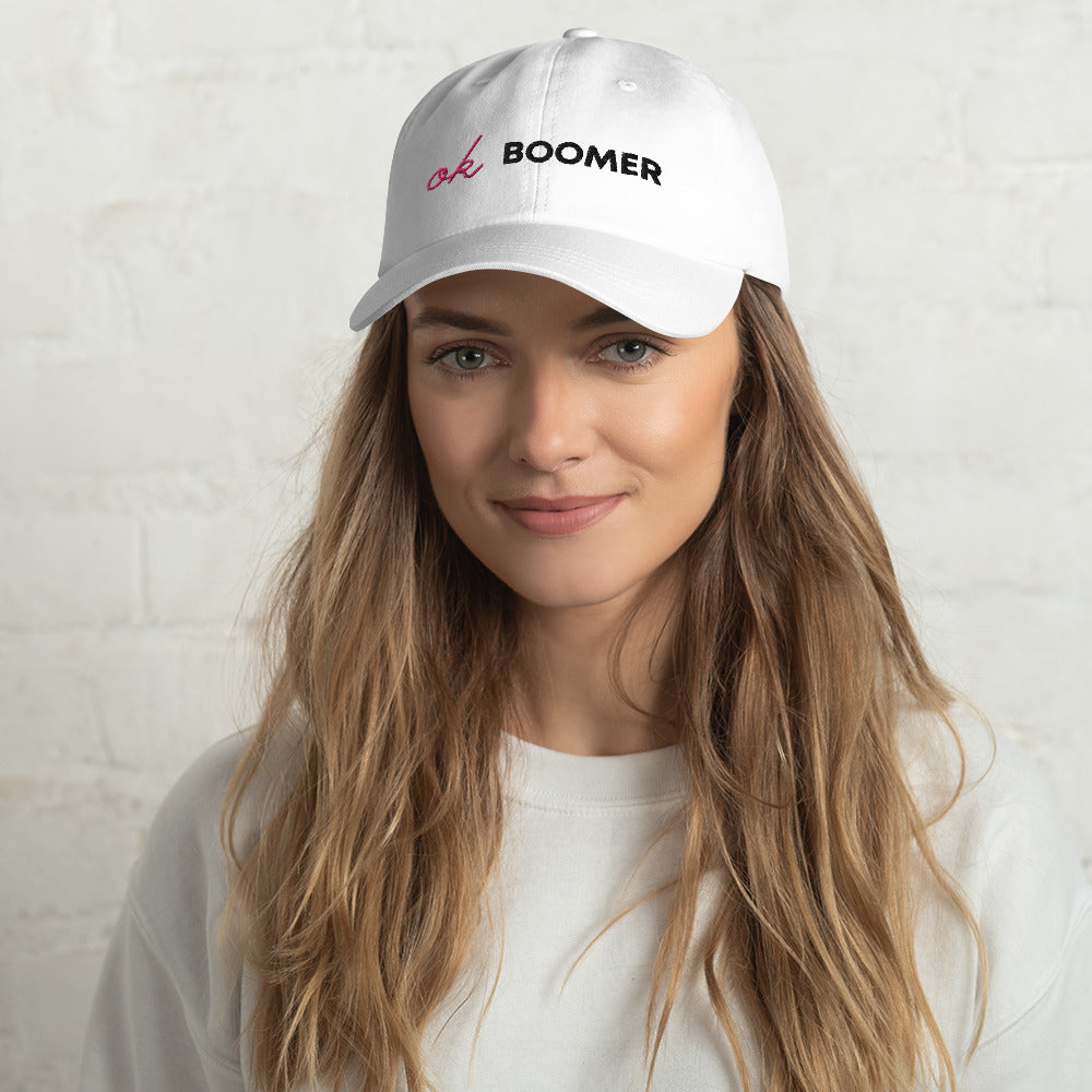 Model wearing a white cap embroidered with pink and black “ok BOOMER” text